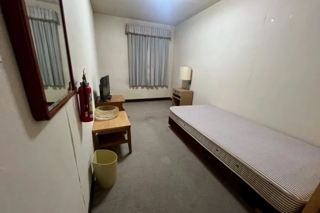 リゾートバイトの個室寮の室内。ベッド、テレビ、テーブル、スタンドライトが備え付けられており、生活に必要な家具家電が揃っている。