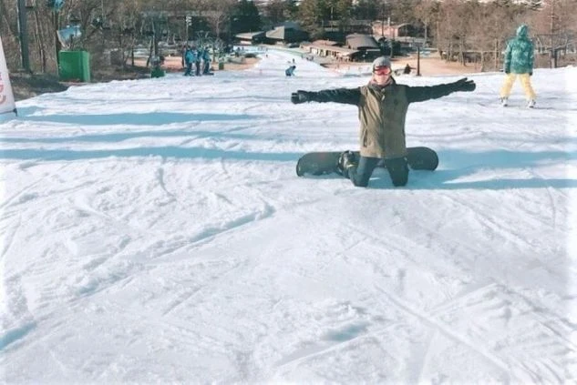 雪の上に立って両手を広げている男性スノーボーダーの画像。