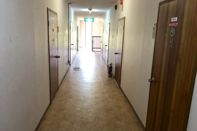 リゾートバイトの寮にある廊下。個室のドアが並び、奥には共用スペースへ続く階段が見え、住み込み生活の様子をイメージできる。