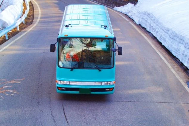 雪の残る山道を走る青い送迎バスの画像。