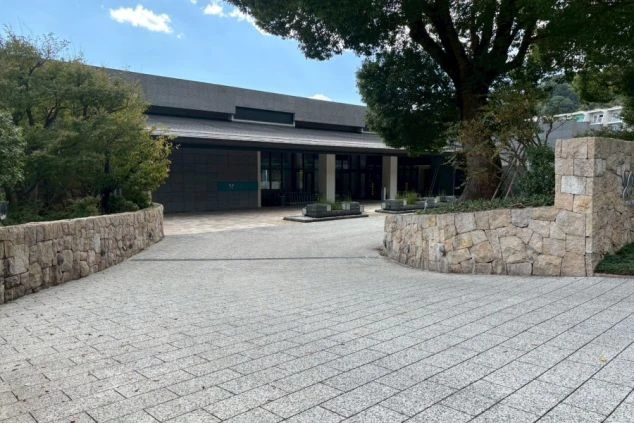 エントランス。積み上げた石垣にホテルのロゴ（蝶のマーク）が刻まれたサインがあり、その奥に低層でモダンなデザインの建物が見える。