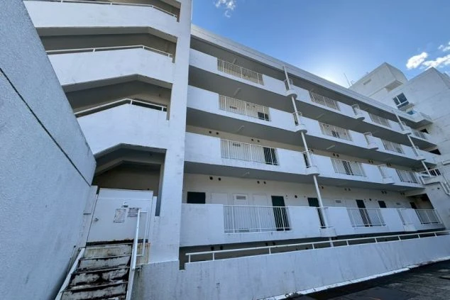 寮の外観。白を基調としたマンションまたはアパートのような建物で、各階に長いバルコニーがあり、階段が外部に設置されている。