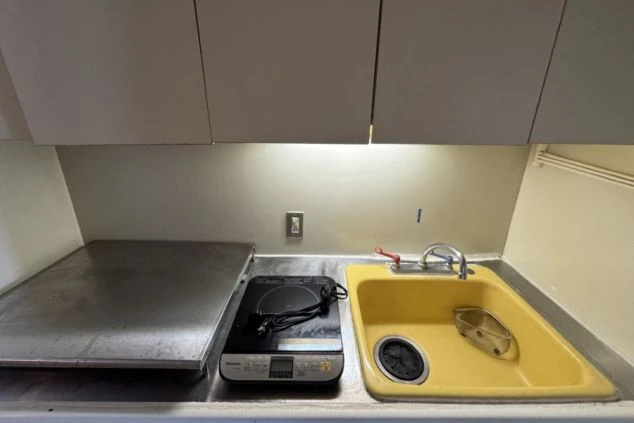 寮のミニキッチン。黄色いシンクと一口IHクッキングヒーターが設置された調理台。上部には収納棚がある。