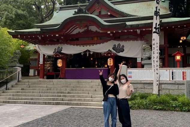 2人の女性ワクトリスタッフが、神社の前で笑顔でピースサインをしている画像。リゾートバイトの休日に観光を楽しんでいる様子が伝わるオリジナル画像。