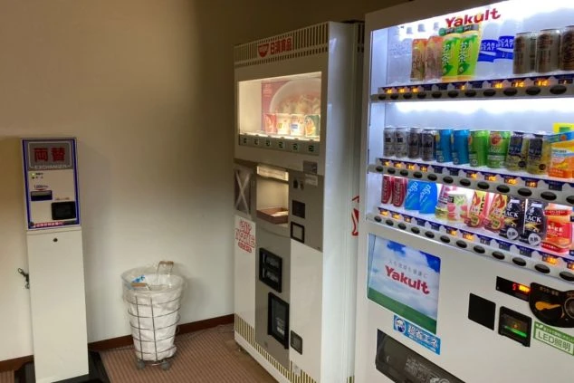 リゾートバイトの寮の共用スペースにある、自動販売機と両替機の画像。飲料水やカップ麺が販売されており、生活に役立つ設備が揃っている。リゾートバイトの寮の共用スペースの画像。