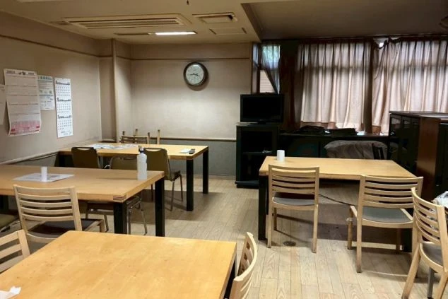 リゾートバイトの寮の共用スペースの画像。複数のテーブルと椅子が置かれており、掲示板が設置されている。リゾートバイトの休憩時間や食事の時間を過ごす、従業員食堂の画像。