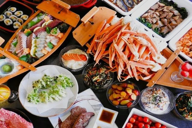 カニや刺身、ステーキなどが並ぶ、豪華なビュッフェ料理の写真。リゾートバイトでは、このような料理の調理補助として勤務することを伝えている。