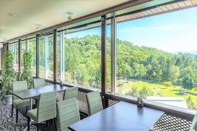 窓の外に広がる緑豊かな森の絶景を眺めながら食事ができる、ホテルのレストランの写真。