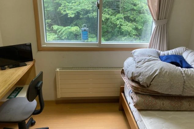 リゾートバイトの寮の部屋の中を撮影した画像。窓からは緑豊かな自然が見え、ベッドとデスクが置かれている。リゾートバイトの寮の部屋の画像