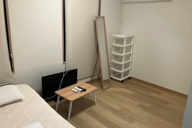 寮の個室。ベッド、テレビ付きの机、姿見、収納ケースが映る。