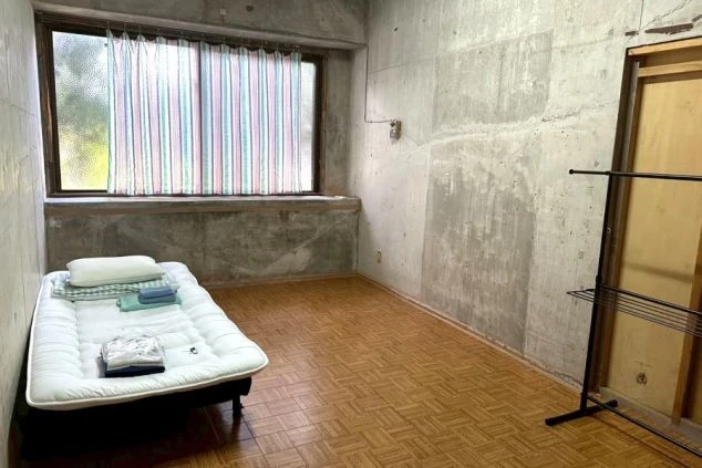 リゾートバイトの寮の個室。コンクリートの壁とフローリングのシンプルな部屋に、ベッドが備え付けられています。