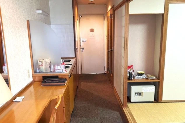 寮の玄関。机、金庫、収納棚がある個室の入り口が映る。