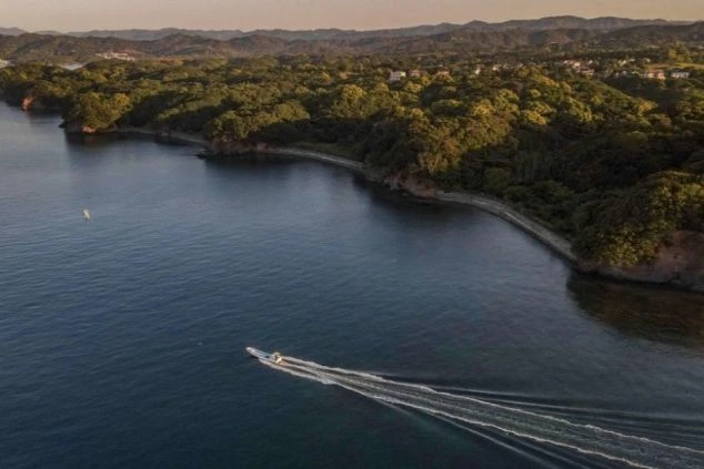 建物の正面。大きな瓦屋根と黒い壁のモダンな和風建築で、全面ガラス戸の向こうに室内が見える。手前は手入れされた芝生で、飛び石がある。