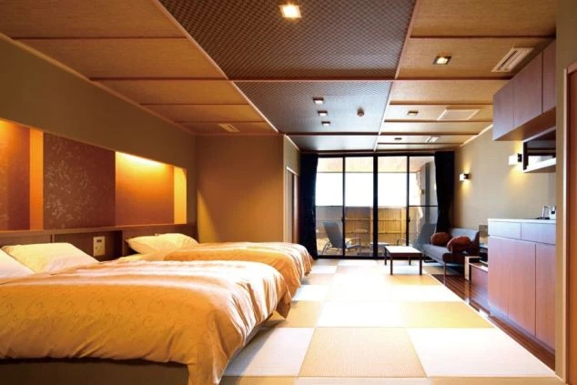 温泉旅館の客室。畳とフローリングが融合した和洋室で、ツインベッドやソファが置かれている。窓の外にはテラスがあり、リゾートバイトの寮や客室の快適さをアピール。