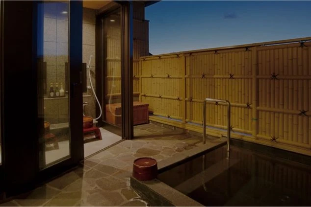 温泉旅館の客室にある露天風呂。竹垣で囲まれた空間に岩風呂があり、桶や椅子が置かれている。リゾートバイトの休日に、プライベートな温泉を楽しめる特典をアピール。