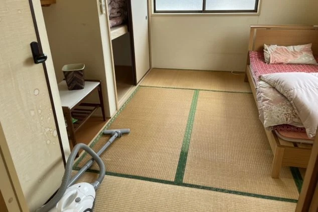 リゾートバイトの寮の和室。畳の部屋にベッドが置かれ、奥には布団が収納された押し入れがある。