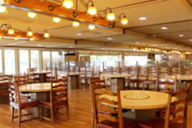 ゴルフ場のレストラン。複数のテーブルと椅子が並び、木目調の内装が温かみのある空間を演出。ホール・レストランサービスのリゾートバイトの仕事場をイメージさせる。