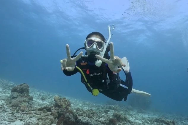 ワクトリでリゾートバイトをしたスタッフが撮影した、沖縄の海中で、スキューバダイビングを楽しむ女性。カメラに向かってピースサインをしており、マリンアクティビティの仕事や、休日のダイビング体験をアピール。