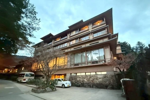 夕暮れの空の下、石垣の上に建つ、和風建築の重層的な建物と、手前に駐車された車。