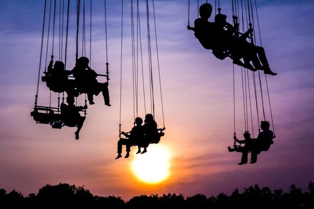 夕焼けを背景に、ブランコのような乗り物に乗って遊んでいる人々のシルエット。