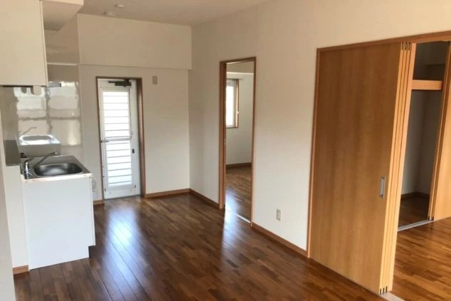 リゾートバイト寮の室内。フローリングの床で、キッチンと洋室、クローゼットが見える。明るく清潔感のある空間。