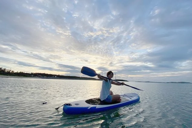 沖縄の海沿いに立つリゾートホテル。エメラルドグリーンの海と白い砂浜、緑の木々が広がり、ホテルのプールも見える。リゾートバイトの勤務地として、最高のロケーションをアピール。