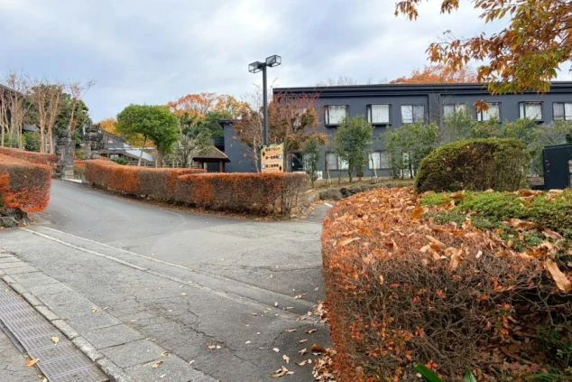 バリ風の黄色い傘と石像が置かれた、アンダの森 伊豆いっぺき湖の入口。奥にはシックな黒い外観の宿泊棟が見えます。