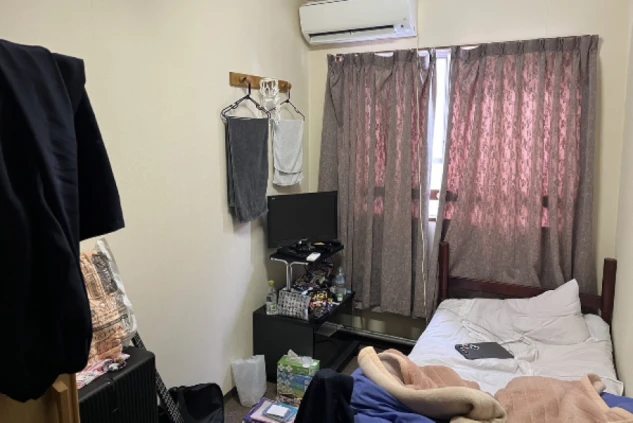寮の個室。ベッド、テレビ、エアコンのある部屋が映る。