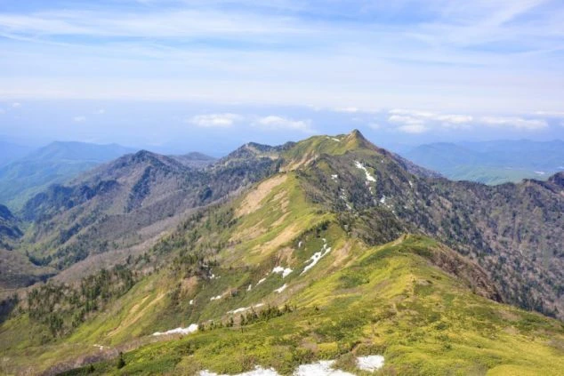 リゾートバイトの休日に登山するイメージ画像。どこまでも続く稜線と、雪解けの跡が残る山々の風景。