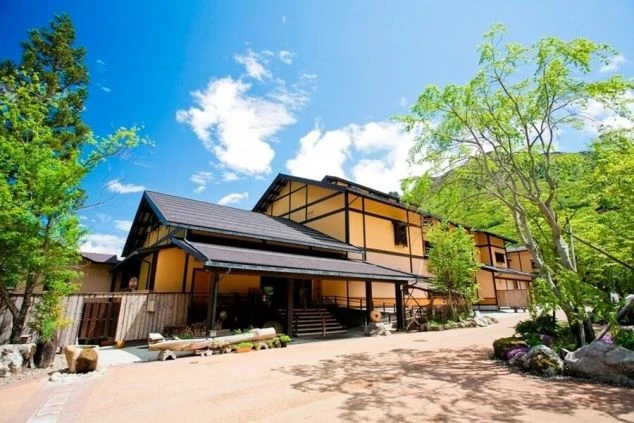 和風の建物が建つ、リゾート地の風景の画像。青空の下、緑豊かな山々に囲まれた、和風のホテルの外観の画像。