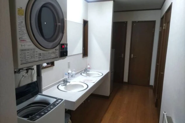共同洗面所とランドリースペースの画像。ドラム式と縦型の洗濯機、2つの洗面台があり、清潔感がある。リゾートバイト中の生活に便利。