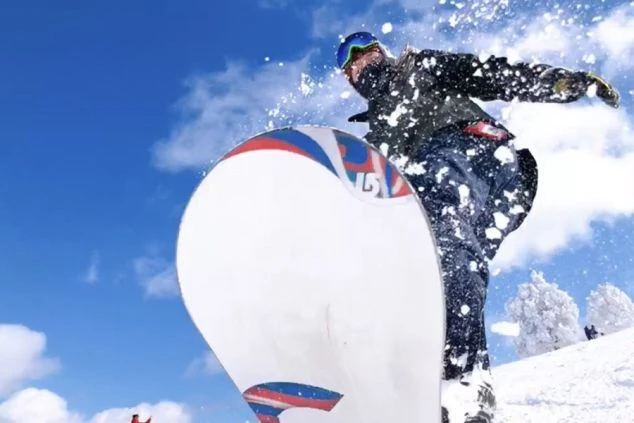 スノーボードウェアを着用した男性が、青空の下で高くジャンプしている画像。雪しぶきが舞い上がり、スノーボードを楽しんでいる様子が伝わってくる。リゾートバイトの休日の過ごし方やアクティビティを表す画像。