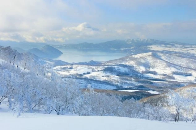 雪化粧をした山々を上空から撮影した画像。雪原の奥には湖が広がり、美しい冬の景色が楽しめる。リゾートバイトの休日に観光を楽しめる、自然の風景の画像。
