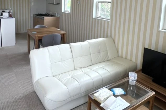 白のレザーソファとローテーブルが備え付けられた、ゆったり寛げるリゾートバイトの個室寮のリビングの画像。