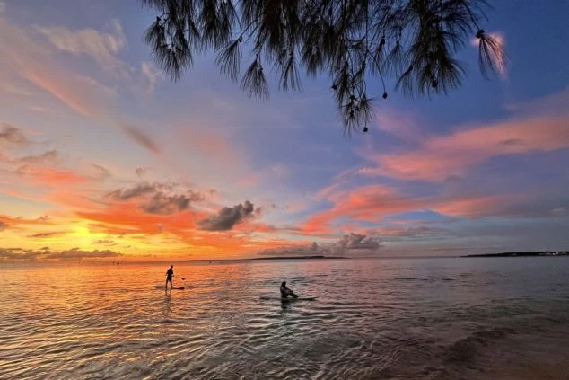 夕焼けに染まる海辺でSUPを楽しむ人。リゾートバイトの休日には、美しい景色を眺めながらマリンアクティビティを満喫できます。
