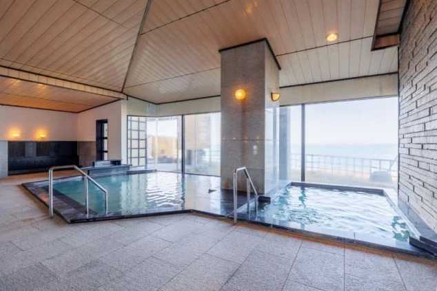 リゾートバイトの仕事先の温泉施設のイメージ画像。窓から海が一望できる、開放感のある内風呂。