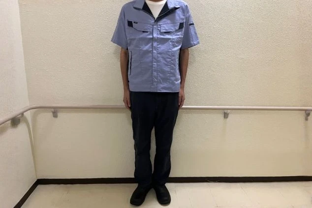 薄い水色の半袖作業着と濃紺のパンツを着用した男性スタッフの全身画像。スチュワードや洗い場業務に適した清潔感のある制服。