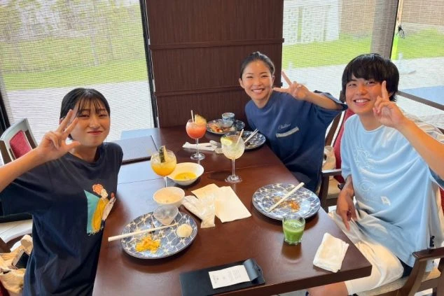 沖縄のホテルレストランで食事を楽しむ若者たち。南国風のドリンクや料理を囲み、リラックスした笑顔で談笑。ワーケーションで訪れた際のランチや夕食の様子。