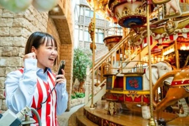 遊園地のスタッフが、トランシーバーを持ち、メリーゴーランドの前で笑顔で立っている画像。遊園地やアトラクションでのリゾートバイトの仕事内容を表す画像。