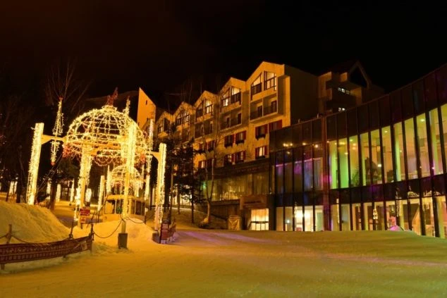 ライトアップされた冬のリゾートホテルの夜景の画像。雪に覆われた道にイルミネーションの温かい光が灯り、幻想的な雰囲気を醸し出している。リゾートバイトの仕事場となるホテルの外観の画像。