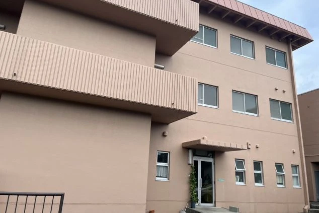 ピンクがかったベージュの外壁が特徴的な3階建ての寮の外観。