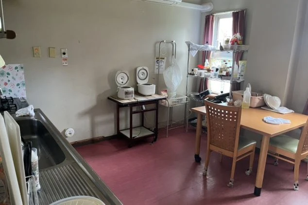 炊飯器、電子レンジ、流し台、ダイニングテーブルが置かれた、寮の共用キッチン兼ダイニング。