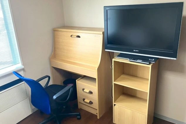 小さなテレビと3段のプラスチック収納ケースが置かれた寮の室内の画像。
