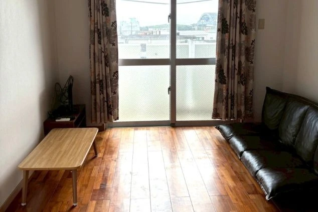 石垣島リゾートバイトの個室寮。バルコニー付きの明るい洋室で、ソファやテーブルも備わった寛げる室内。