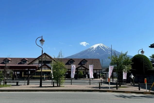 青空のもと、雄大な富士山を背景にした富士急行線「河口湖駅」の駅舎とロータリー。富士河口湖温泉郷など、山梨県の人気観光地で働くリゾートバイトの赴任先イメージ。