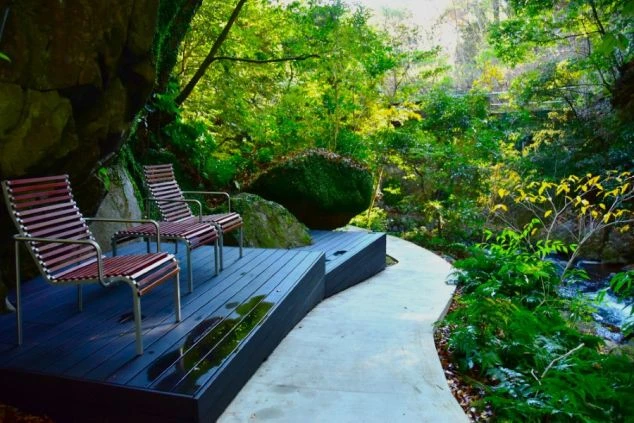 湯河原の豊かな自然に囲まれたリゾート施設の休憩スペース。川のせせらぎが聞こえるウッドデッキに並ぶモダンなテラス席。仕事の合間にリフレッシュできる最高の就業環境。