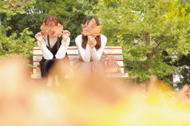 公園のベンチで紅葉の葉を持ち笑顔を見せる女性たち。リゾートバイトは仲間と休日も楽しめます。
