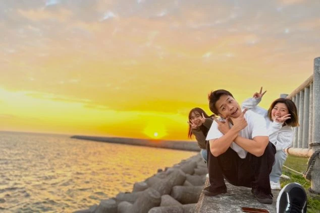 石垣島の海辺で夕日を背景にポーズをとるリゾートバイト仲間の写真。