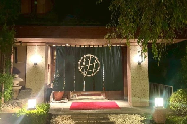 ライトアップされた旅館の玄関。大きな暖簾と赤い敷物が、高級感のある和の雰囲気を演出。