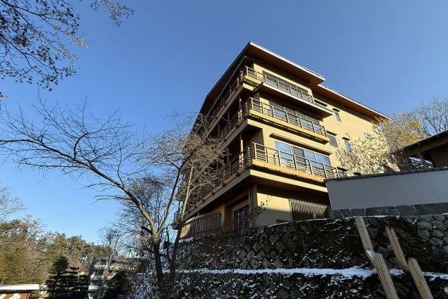 木目調で統一された広々とした旅館のロビー。お客様を案内するスタッフの姿があり、リゾートバイトの仕事風景をイメージさせます。